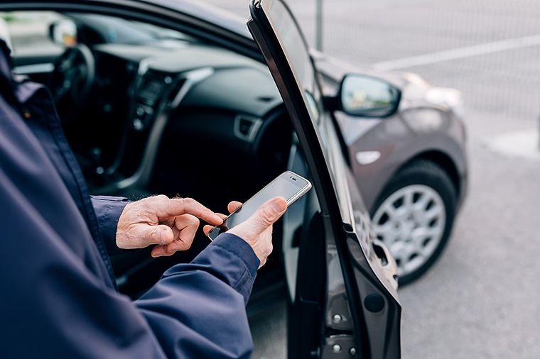 Älterer Mann mit Handy steht vor einem Carsharing-Auto.