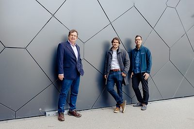 Drei Personen stehen vor einer modernen, geometrisch gemusterten Wand.