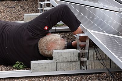 Ein Mann liegt auf dem Boden und arbeitet an einer Solaranlage, die auf Betonblöcken montiert ist.