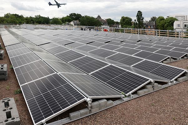 © Mainova Dach mit vielen Solarpaneelen, im Hintergrund fliegt ein Flugzeug über grüne Landschaft.