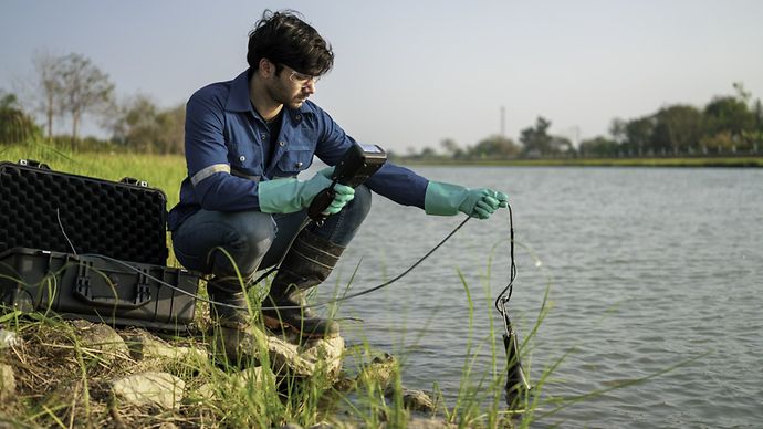 Ein Arbeiter nimmt eine Messung am Flussufer vor.