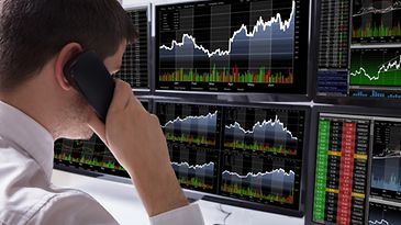 © www.istock.com/AndreyPopov Mann mit Telefonhörer am Ohr beobachtet Aktienkurse auf Bildschirmen