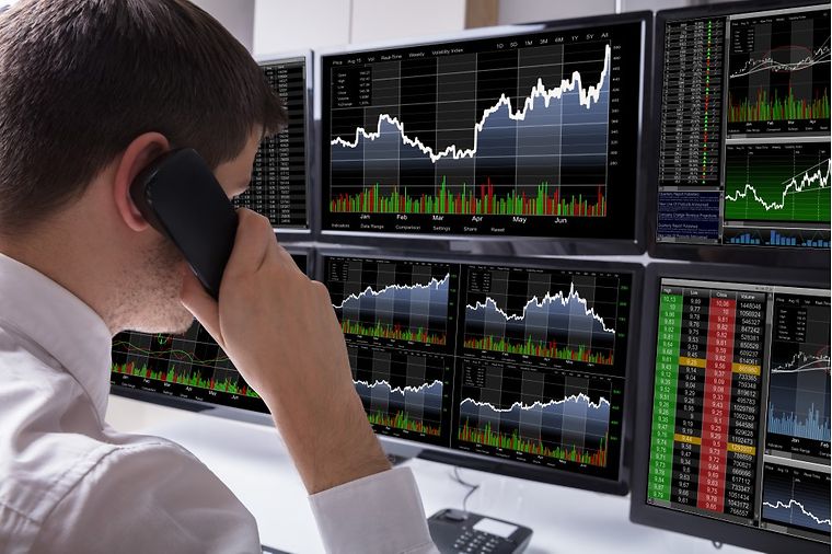 © www.istock.com/AndreyPopov Mann mit Telefonhörer am Ohr beobachtet Aktienkurse auf Bildschirmen