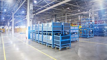 © stock.adobe.com/hacohob Großes Lager mit gestapelten blauen Metallkisten und mobilen Regalen bei guter Beleuchtung.