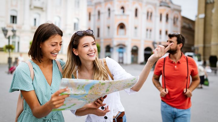 Zwei junge Frauen mit Stadtplan in der Hand betrachten Sehenswürdigkeiten.