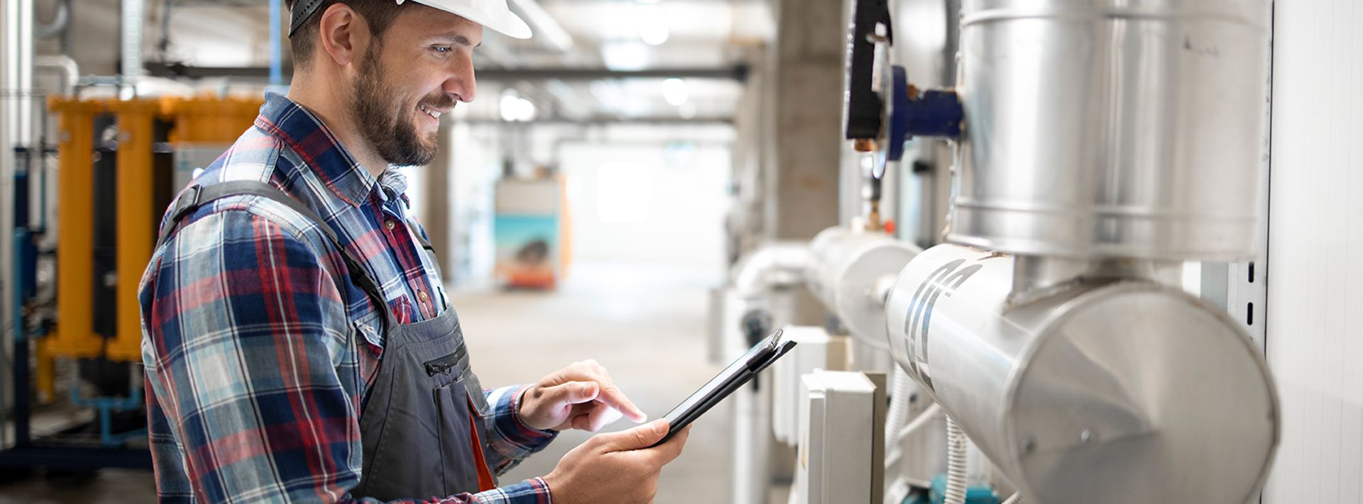 © istockphoto.com/Smederevac Installateur im Heizungraum steht an den Leitungen und prüft mit dem Tablett die Werte