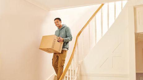 Mann geht mit Umzugskarton eine Treppe hinab