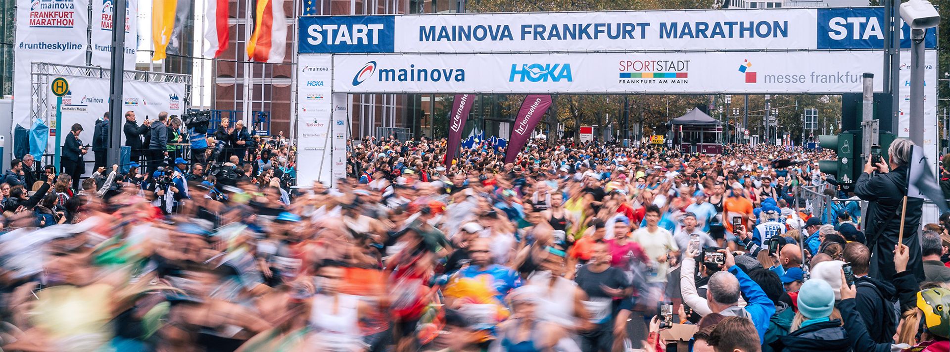 Start des Frankfurt Marathons mit Läufermenge und Zuschauern unter Werbebannern.