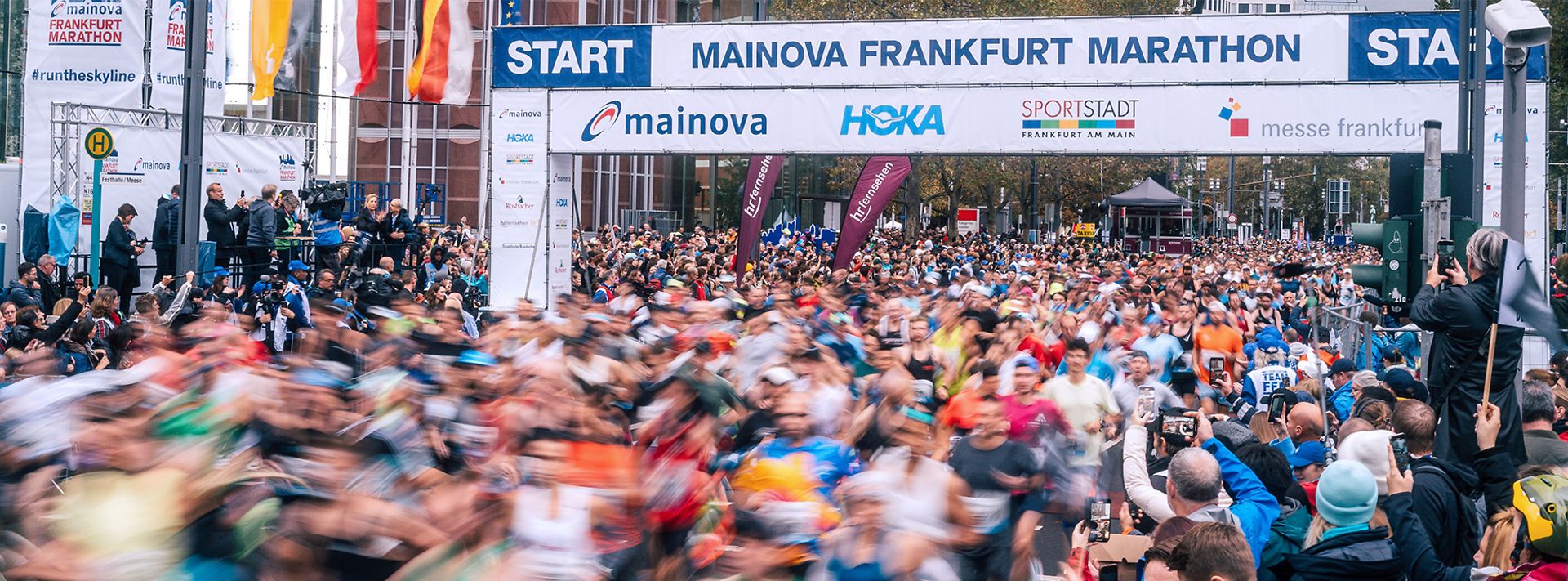 © Sebastian Pociecha Start des Frankfurt Marathons mit Läufermenge und Zuschauern unter Werbebannern.
