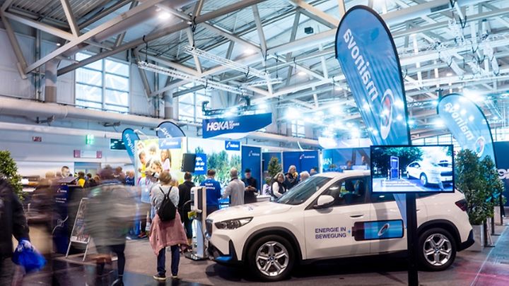 Messehalle mit Besuchern, Ausstellungsauto und "Mainova"-Stand im Fokus.