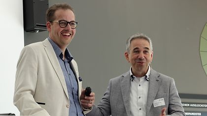 Zwei Personen lachen, die eine hat ein Mikrofone in der Hand 