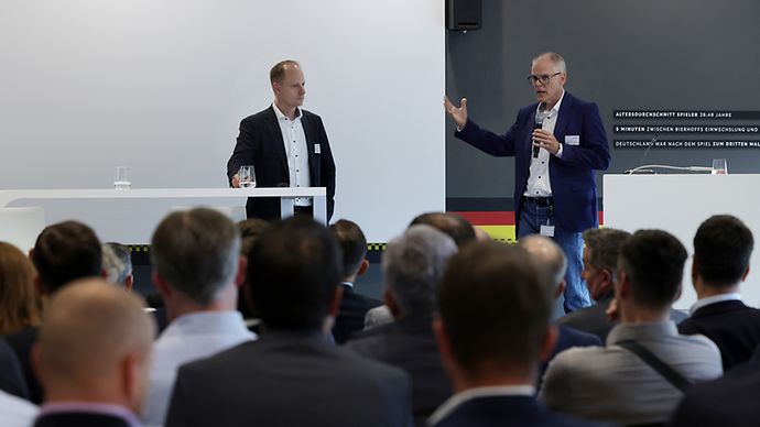 © Mainova Ein Redner spricht auf einer Konferenz, während das Publikum zuhört. Eine Präsentation zum "Tiefbaugipfel" wird angezeigt.