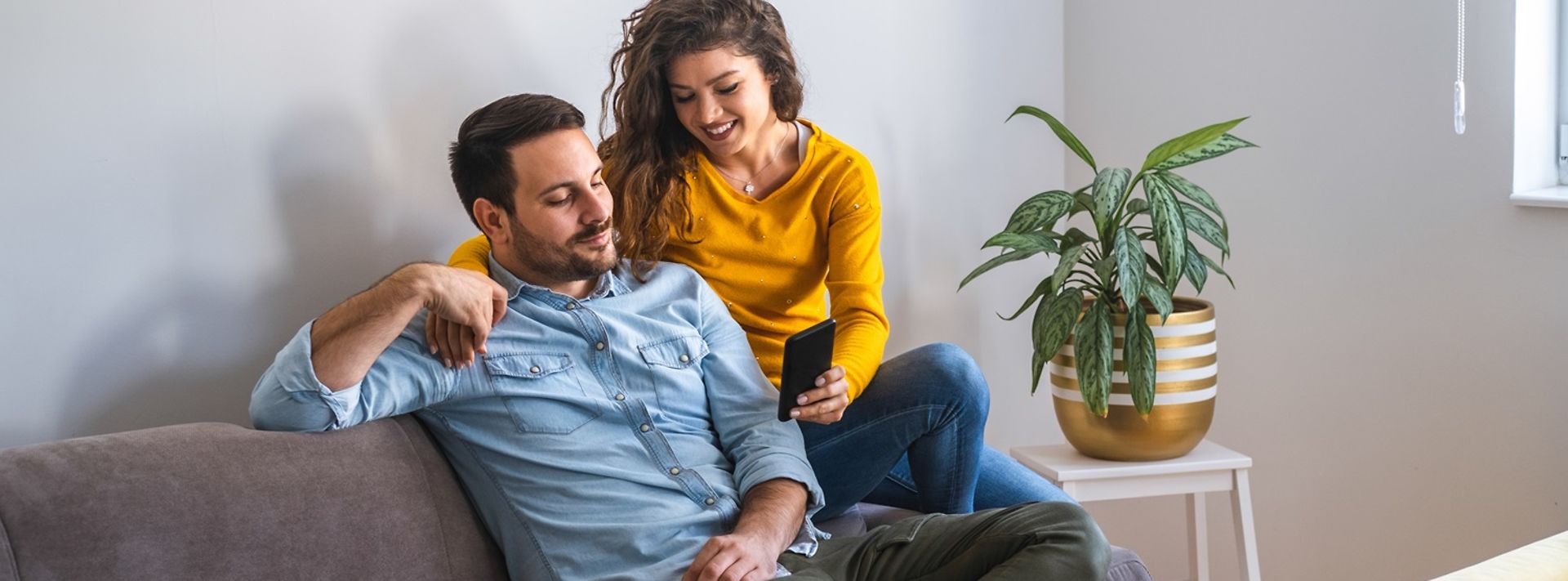 © stock.adobe.com/Tijana Mann und Frau sitzen auf einem Sofa und schauen zusammen auf ein Handy