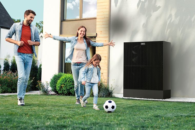 Eltern und Tochter spielen Fußball im Garten, das Mädchen rennt mit Ball vorneweg