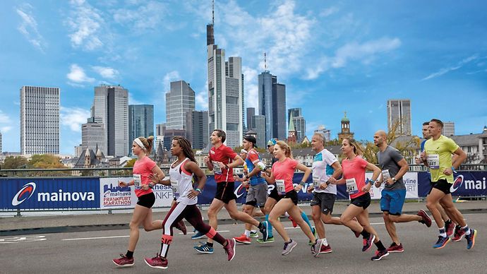 Läufergruppe vor der Frankfurter Skyline und vor Zaun mit Mainova Banner