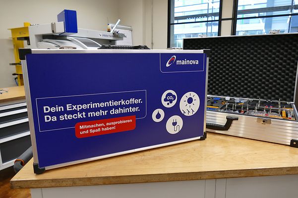 Ein blauer Experimentierkoffer von Mainova, darauf der Text: "Mitmachen, ausprobieren und Spaß haben!"; daneben geöffnet.