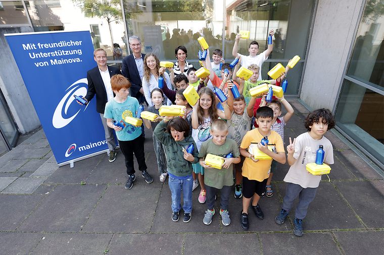 © Heiko Rhode Eine Gruppe von Kindern mit gelben Brotboxen, vier Erwachsene und ein Mainova Aufsteller im Hintergrund