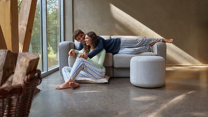 Mann liegt auf Couch und hält seine Frau im Arm, die auf dem Boden sitzt