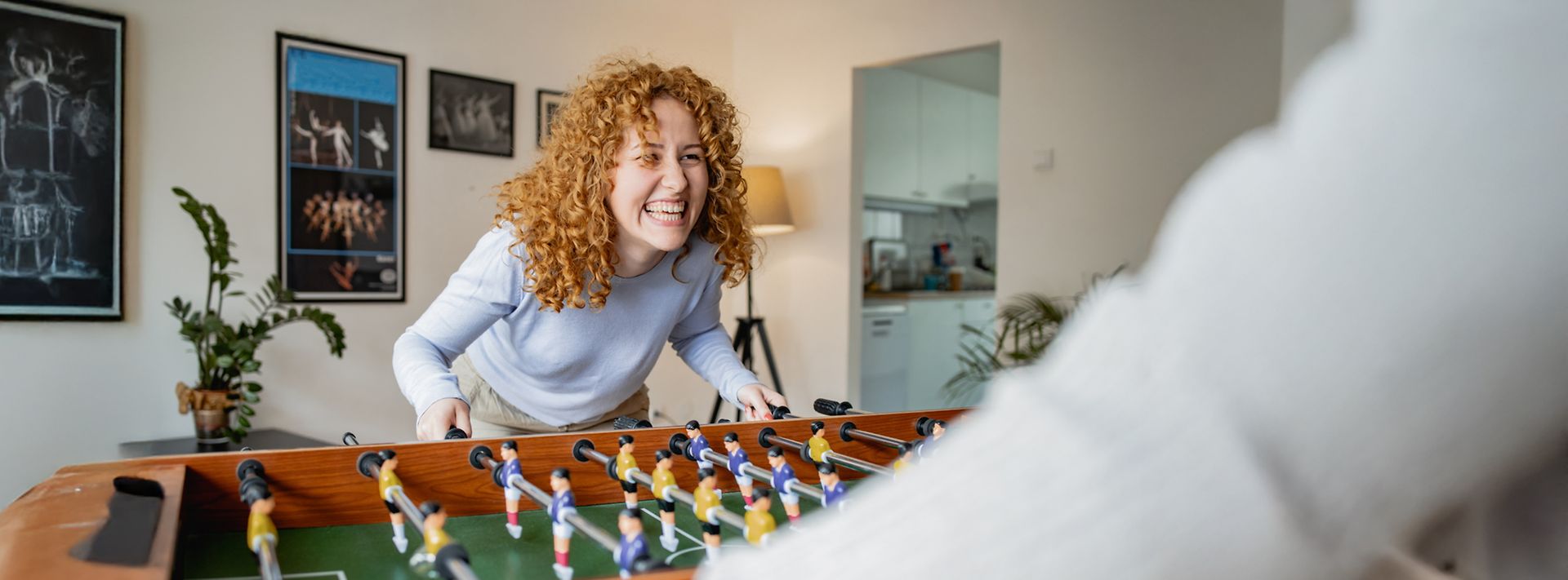 © maca and nara Rothaarige Frau spielt Tischkicker gegen einen Mann und lacht