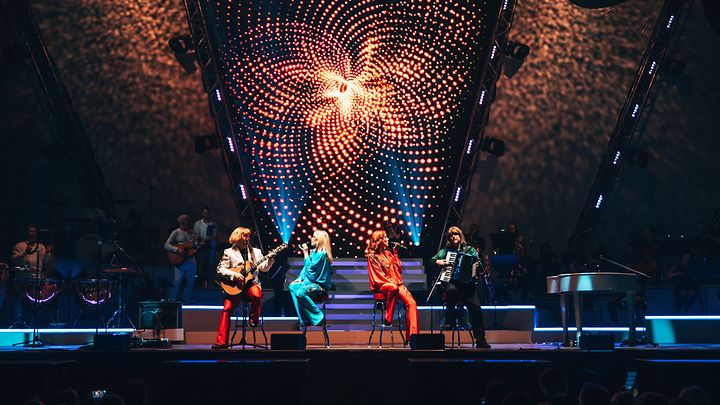 Konzertbühne mit bunter Lichtshow und vier Musiker in farbenfrohen Kostümen