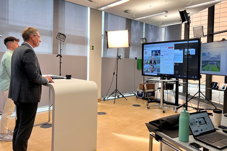 © Mainova Zwei Männer stehen in einem Aufnahmestudio, an Pult und vor großem Bildschirm