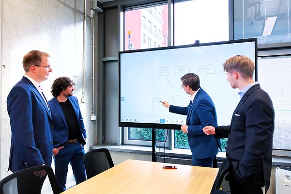 Teammeeting vor einem Bildschirm, auf dem etwas aufgezeigt wird