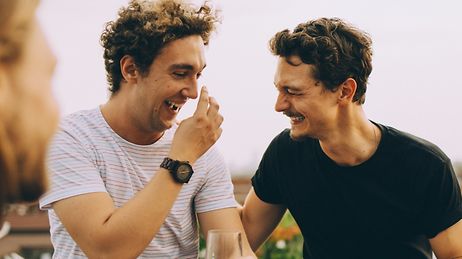 © Maskot Zwei glückliche Männer auf einer Dachterasse lachen zusammen