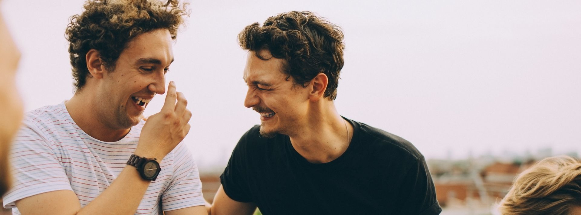 Zwei glückliche Männer auf einer Dachterasse lachen zusammen