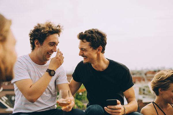 © Maskot Zwei glückliche Männer auf einer Dachterasse lachen zusammen