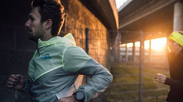 Mann joggt vor Frau bei Sonnenuntergang