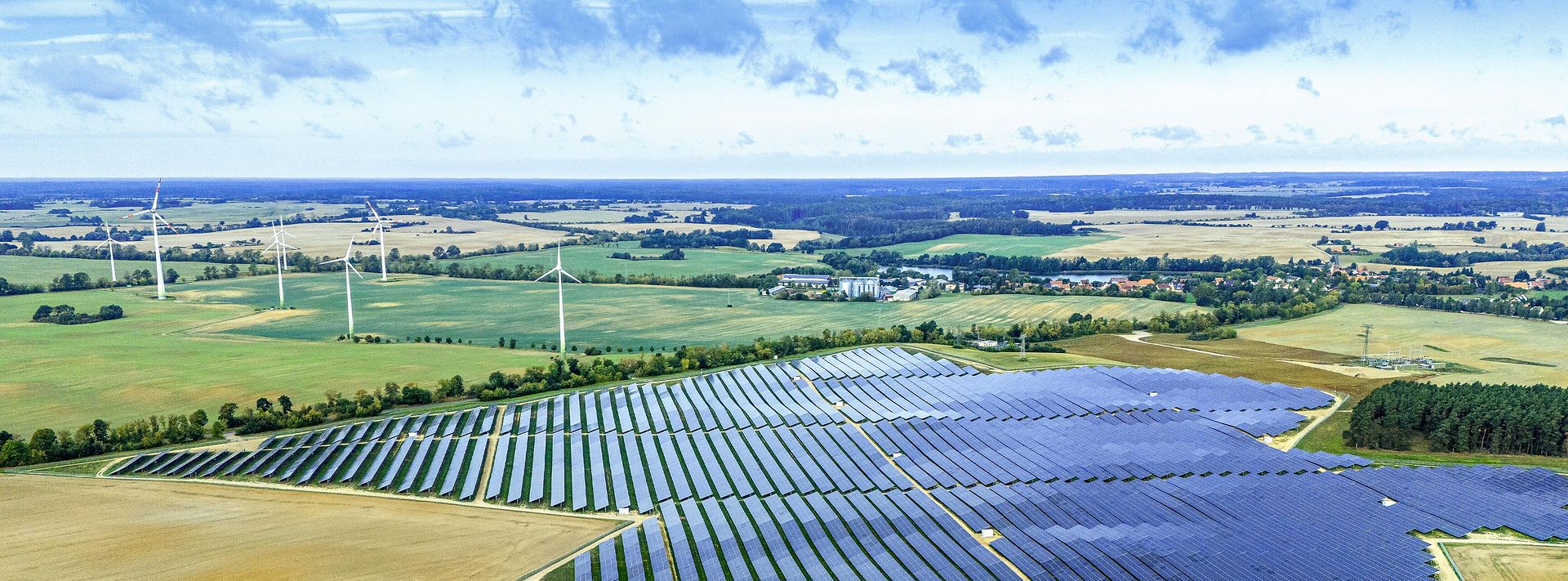 Großer Solarpark mit Windrädern in weiter Landschaft – Symbol für erneuerbare Energie und nachhaltige Stromerzeugung.