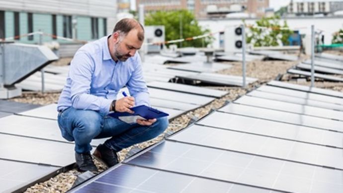 Techniker hockt neben einer Solaranlage auf einem Dach und nutzt ein Tablet zum Prüfen