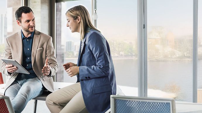 © Westend61 via Getty Images Geschäftsmeeting zwischen Mann und Frau im Büro vor der Skyline Frankfurt.