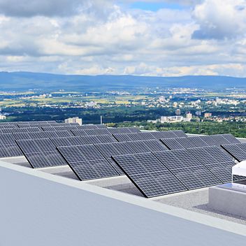 © adobestock/ValThoermer Solaranlagen auf einem Dach mit Blick auf eine Stadt und einen Fernsehturm im Hintergrund.