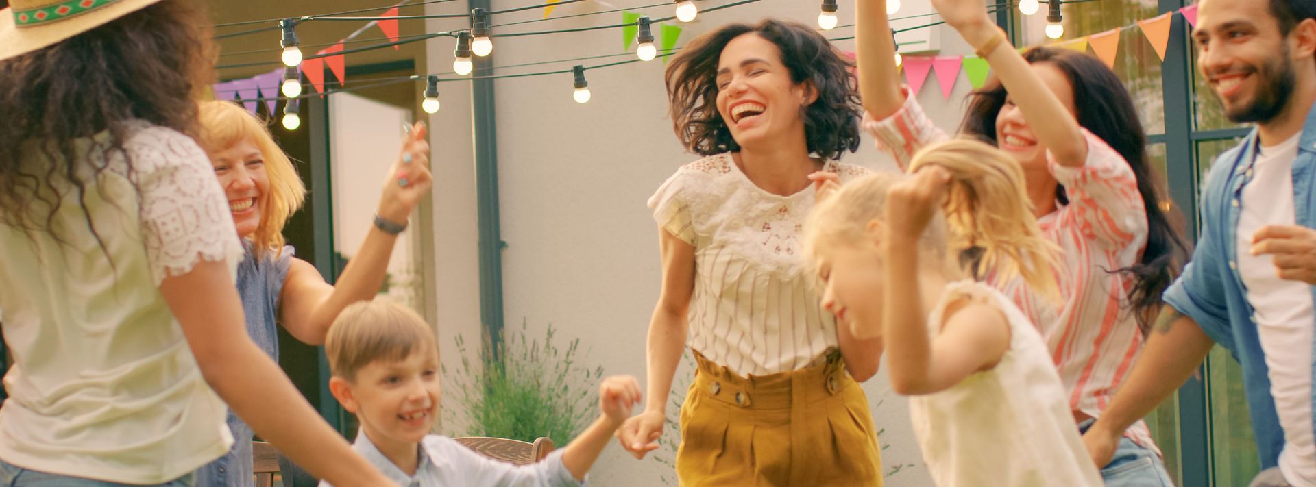 Gruppe tanzt im Garten unter Lichterkette, bunte Wimpel hängen vor einem Wohnhaus.