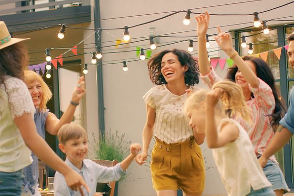 Gruppe tanzt im Garten unter Lichterkette, bunte Wimpel hängen vor einem Wohnhaus.
