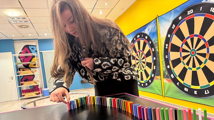 Frau stellt bunte Dominosteine auf und daneben befinden sich Dartscheiben