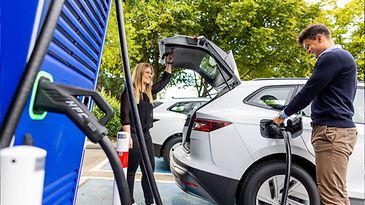 © Dennis Möbus Frau und Mann mit weißem E-Auto an Ladesäule, Mann lädt Auto