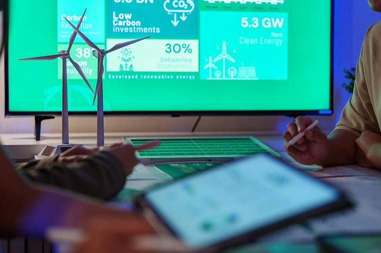 Besprechung zwischen zwei Personen. Auf Bildschirmen werden Daten zu CO2-Bilanzen gezeigt.