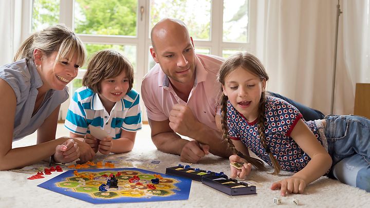 © Franckh-Kosmos Verlags-GmbH & Co. KG Mutter, Vater und zwei Kinder liegen auf dem Boden und spielen ein Brettspiel