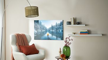 Sessel mit Lampe dahinter und kleinem Tisch und an der Wand ein Foto mit Schneelandschaft