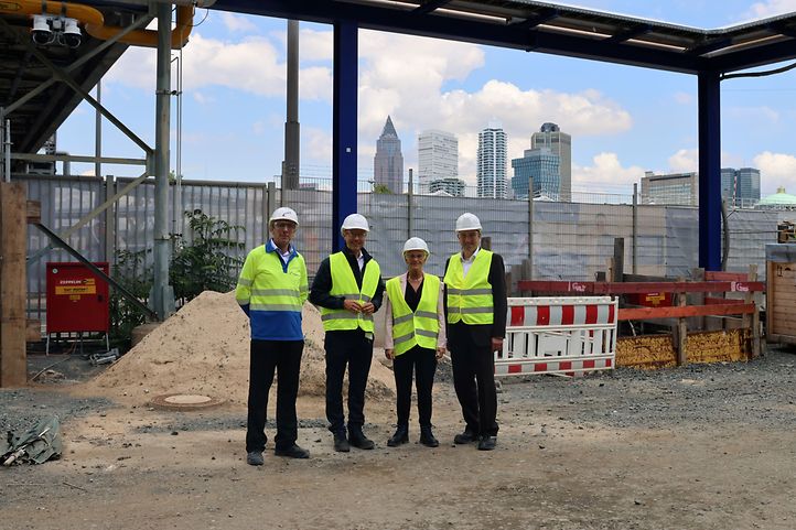 vier Personen in Sicherheitswesten auf einer Baustelle vor der Frankfurter Skyline