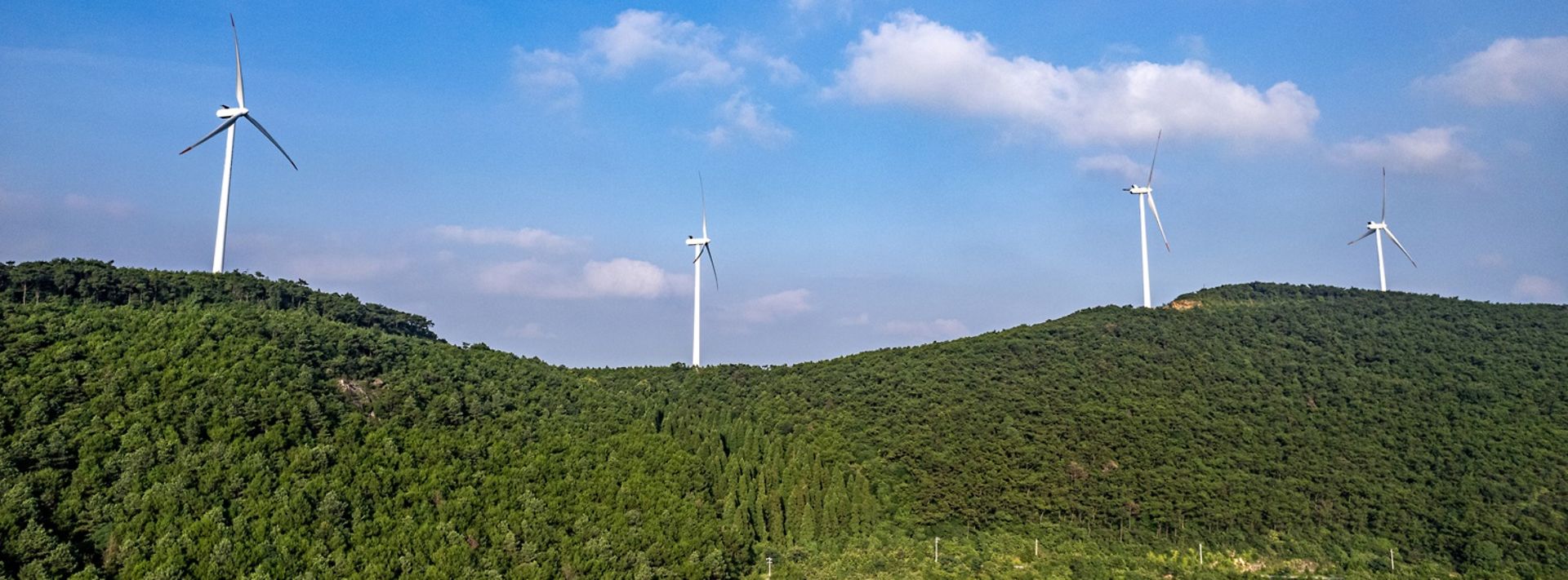 © www.istock.com - su tim 4 Windräder auf einem grünen Hügel. dahinter blauer Himmel