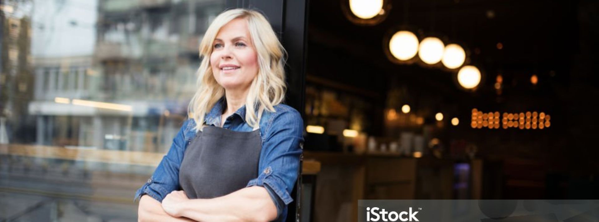 Wirtin seht lächelnd vor ihrem Restaurant, dahinter leuchten die Deckenlampen