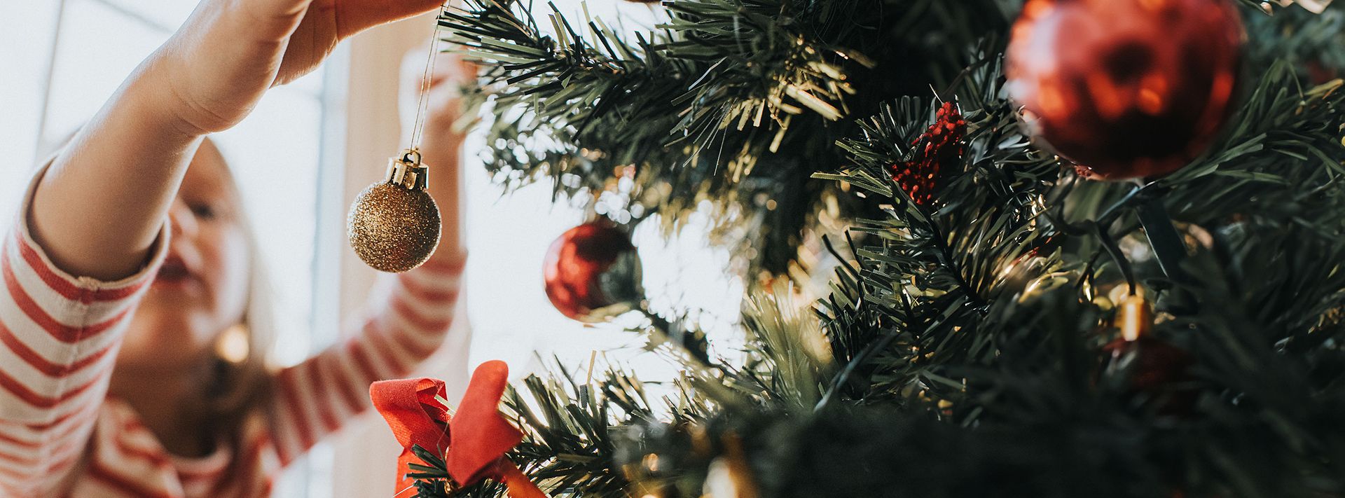 kleines Mädchen hängt eine goldene Weihnachtskugel an den Weihnachtsbaum