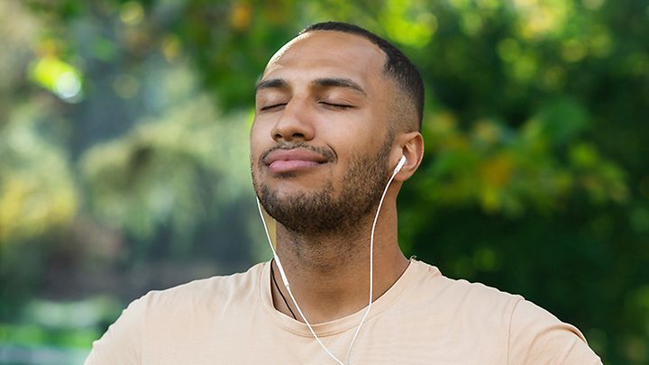 Mann mit Kopfhörern und geschlossenen Augen genießt im Grünen die Musik