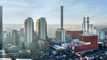 Luftaufnahme eines Industrieareals mit Kraftwerksgebäuden und Schornsteinen, dahinter Stadt und Bahntrassen.