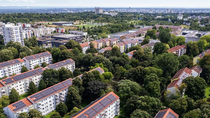 Wohnviertel aus der Luft mit vielen Bäumen und Häusern, deren Dächer teils mit Solaranlagen ausgestattet sind.