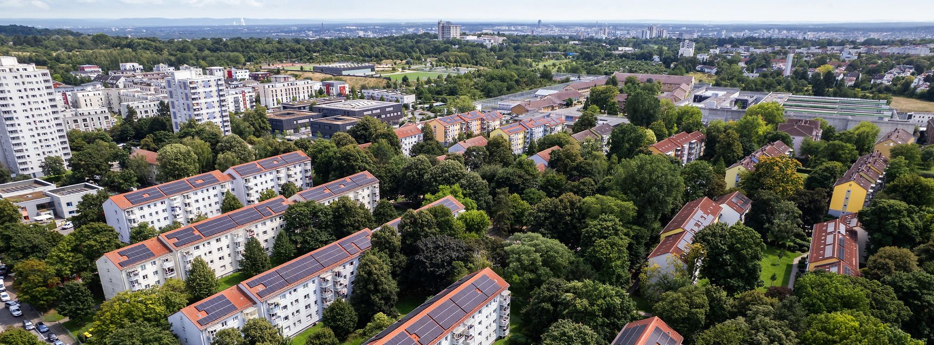 Wohnviertel aus der Luft mit vielen Bäumen und Häusern, deren Dächer teils mit Solaranlagen ausgestattet sind.