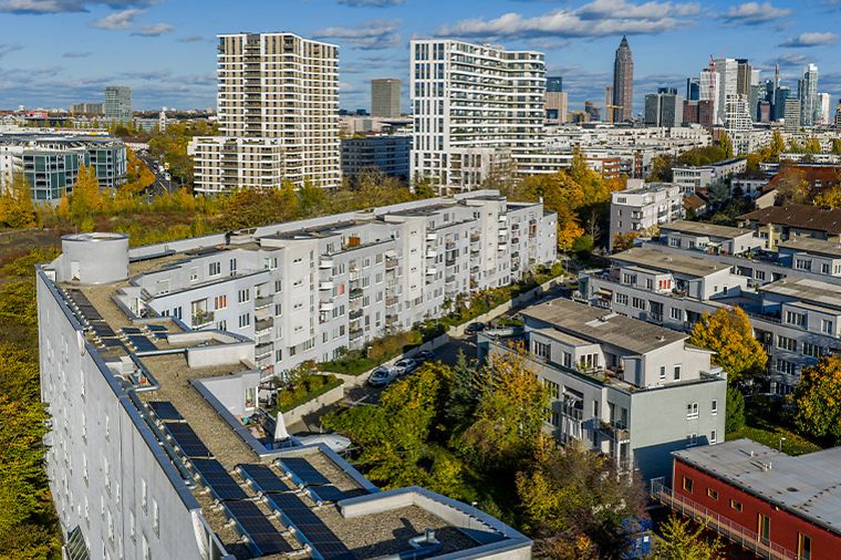 Wohngebäude mit Solaranlagen auf den Dächern vor Frankfurts Skyline und herbstlicher Stadtkulisse.